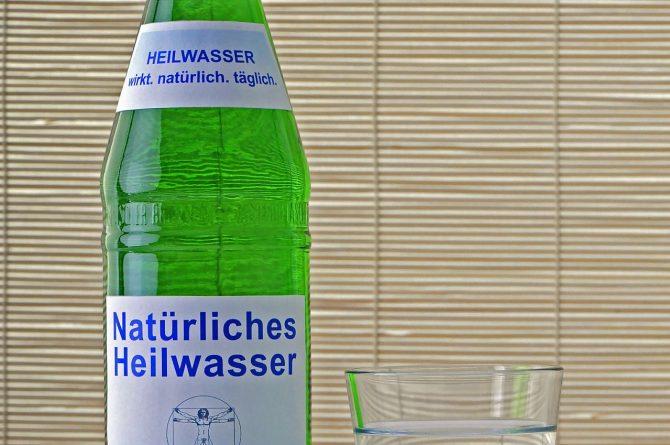 Heilwasserflasche und Glas vor Bambusrollo