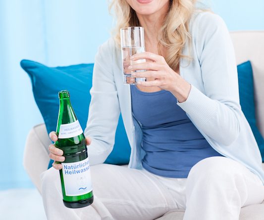 Frau auf weißem Sofa mit Heilwasserflasche_690